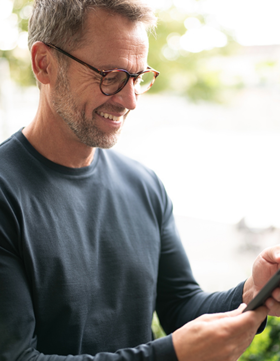 Mann mit Brille blickt auf sein Smartphone.