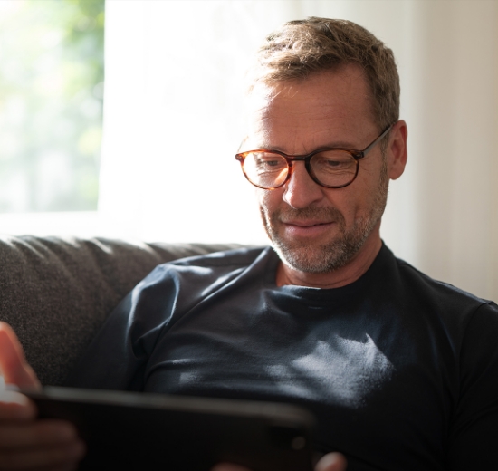 Mann mit Brille sitzt auf dem Sofa und schaut in sein Tablet.